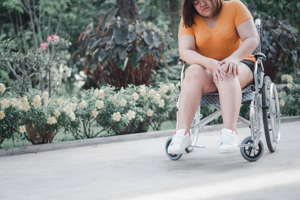 Túlsúlyos és elhízott nő ül a kerekesszékben, és tartja a térdét A fájdalom, oka a gyulladás a térde, hogy túl sok súlyt, koncepciója túlsúlyos probléma és az egészségügyi ellátás - Fotó, kép