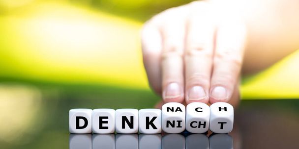 Ręka obraca kości i zmienia niemieckie wyrażenie "denk nicht" (nie myśl) na "denk nach" (myśl). - Zdjęcie, obraz