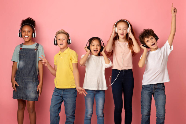 Πολυεθνική μαθητές σε ακουστικά ακούγοντας μουσική ή ακουστικά βιβλία σε ροζ φόντο - Φωτογραφία, εικόνα