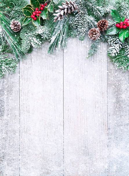 Christmas and New Year background with fir branches, holly and snowfall on wooden white board - Photo, image