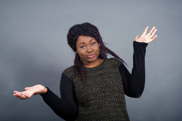 Африканская американка в повседневной одежде с сомнительным выражением лица, смущает и удивляет концепцию, неопределенное будущее пожимает плечами, стоя против серой стены. - Фото, изображение