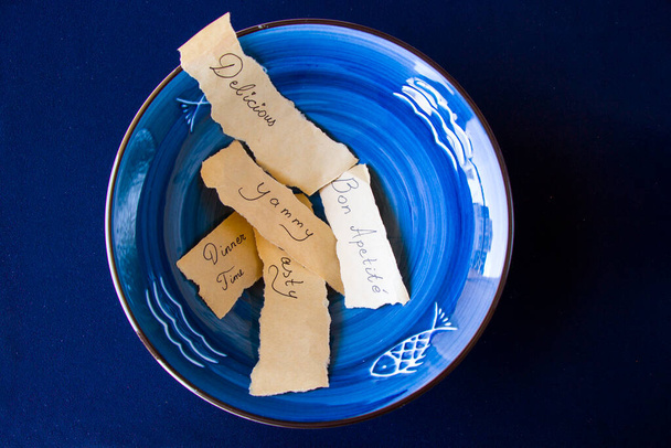 Lecker, köstlich, Abendessen Buchstaben und Text, leeres blaues Geschirr, Schüssel und Teller auf dem blauen Tisch. Tellerset vorhanden. Tisch gedeckt. - Foto, Bild