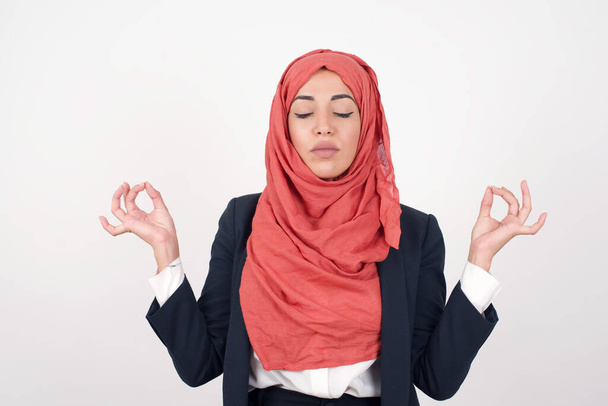 Διαλογισμός, θρησκεία και πνευματικές πρακτικές. Όμορφη μουσουλμάνα γυναίκα φοράει μαύρο σακάκι και μαντίλα, κρατώντας τα μάτια κλειστά, κρατώντας τα δάχτυλα σε χειρονομία mudra. - Φωτογραφία, εικόνα