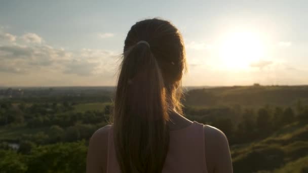 jonge vrouw in de zomer jurk staande in groene weide genieten van zonsondergang uitzicht in de avond natuur. - Video