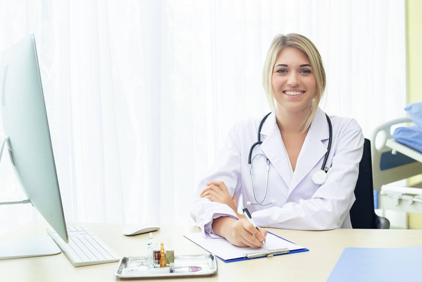 Orvos nő barna haj fehér gyönyörű sztetoszkóppal viselje egyenruha nézi kamera ül munkaasztal a kórházban. az egészségügyi ellátás fogalma. - Fotó, kép