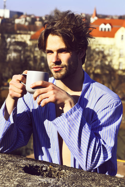 Caucasian macho in blue striped pajamas holding cup - Foto, afbeelding