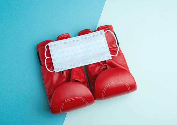 ζευγάρι δερμάτινα γάντια πυγμαχίας και μάσκα προσώπου μίας χρήσης, ιδέα για πανδημικά αθλήματα, κορυφαία άποψη - Φωτογραφία, εικόνα