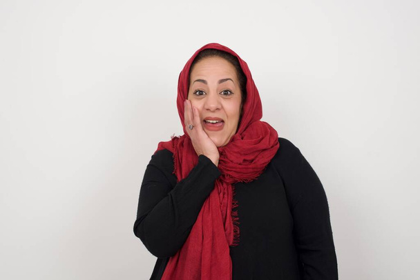 驚いたイスラム教徒の女性は,顔に近い手で完全に信じられないほどの広い口に驚きました. ポジティブな感情の表情ボディランゲージ. スタジオでポーズするヘッドスカーフを身に着けている中年のアラブ女性 - 写真・画像