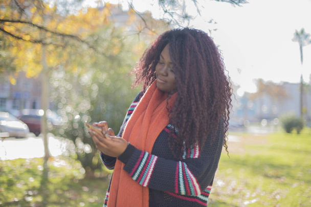 piękna Afroamerykanka z długimi włosami nosząca kolorowy sweter w jesiennym parku   - Zdjęcie, obraz