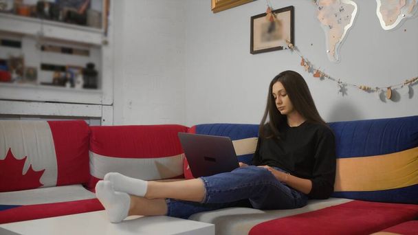 Vakava nuori nainen kirjoittamalla kannettavan tietokoneen selailu chattailuun internetin käyttö app istua sohvalla kotona - Valokuva, kuva