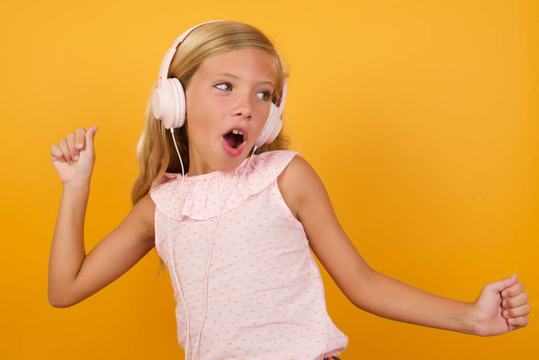 roztomilý holčička v růžových šatech proti žluté studio pozadí ve sluchátkách   - Fotografie, Obrázek