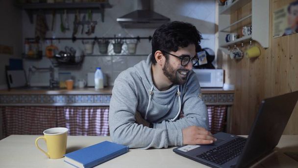 Happy young businessman working on laptop in kitchen at home at night - Foto, Imagem