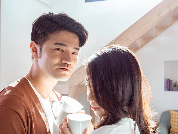 Молода азіатка і чоловік насолоджуються проведенням часу вдома разом з чашкою кави в руках
. - Фото, зображення