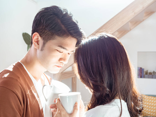 Joven asiático mujer y hombre están disfrutando de pasar tiempo juntos en casa con taza de café en las manos. - Foto, Imagen