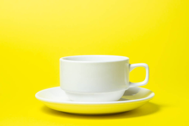 empty cup on a saucer on a yellow background. The cup and saucer are white. A tea set - Fotó, kép