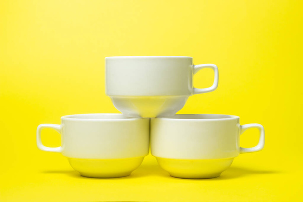 Weiße Tassen auf gelbem Hintergrund. Drei weiße Becher haben die Form einer Pyramide. Ein Tee-Set. - Foto, Bild