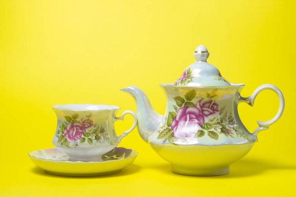 Set de té sobre fondo amarillo. Una taza, un platillo y una tetera al lado. Set de té con decoraciones de flores - Foto, Imagen
