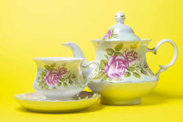Set de té sobre fondo amarillo. Una taza, un platillo y una tetera al lado. Set de té con decoraciones de flores - Foto, imagen