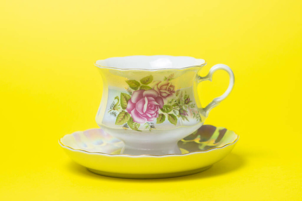 Tazza da tè e piattino su sfondo giallo. Il servizio è decorato con fiori. - Foto, immagini