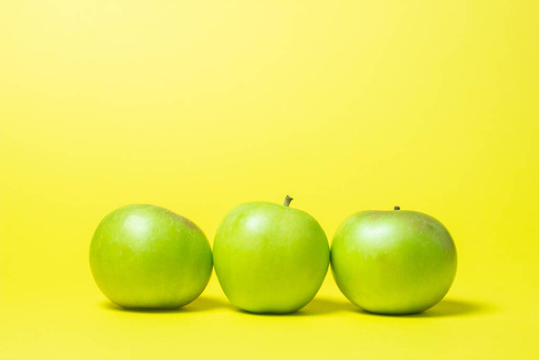 Τρία πράσινα μήλα σε κίτρινο φόντο. Τα μήλα είναι στη σειρά.. - Φωτογραφία, εικόνα