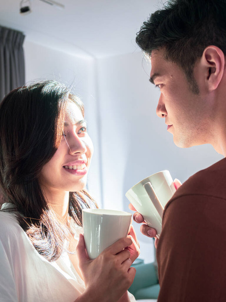Jeune asiatique homme et femme à la maison avec tasse de café dans les mains. - Photo, image