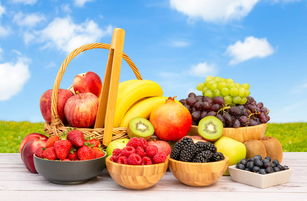 Gruppe Gesundes frisches Obst in einem Holzkorb, mit Vitaminen c aus Bananen, Kiwi, Trauben, Himbeeren, Blaubeeren und Brombeeren, gut für den Körper und Nahrung auf dem Tisch in der Natur Hintergrund. - Foto, Bild
