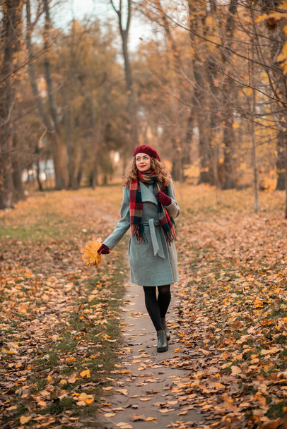 Girl on fabulous background of park with orange autumn leaves in hands walking on road. Pretty stylish smiling woman - Photo, image