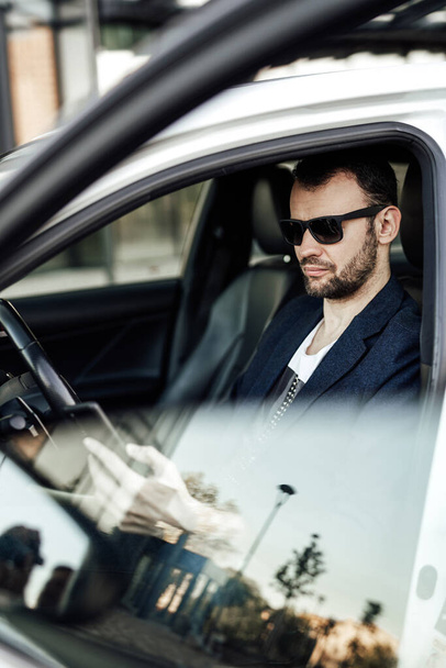 Μόδα πλούσιος άνθρωπος κοιτάζοντας το τηλέφωνο και κάθεται στο αυτοκίνητο - Φωτογραφία, εικόνα