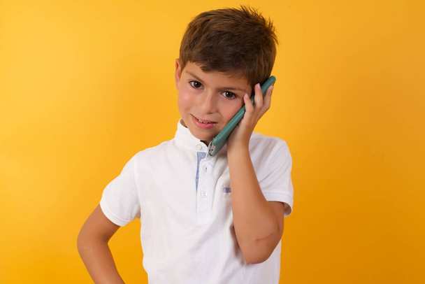 cute boy    talking on smartphone  against yellow  wall   - Fotografie, Obrázek