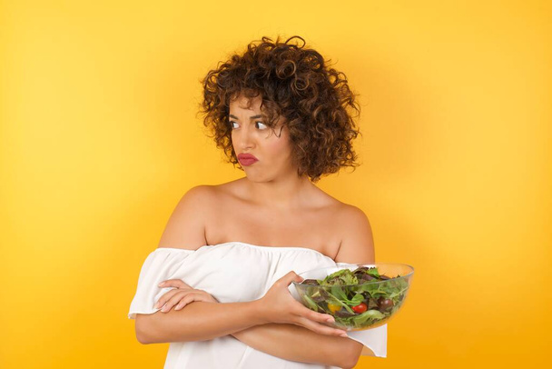 Closeup portrait displeased pissed off angry grumpy pessimistic woman holding a salad dressed casual with bad attitude, arms crossed looking sideways. Negative human emotion facial expression feelings - Photo, Image