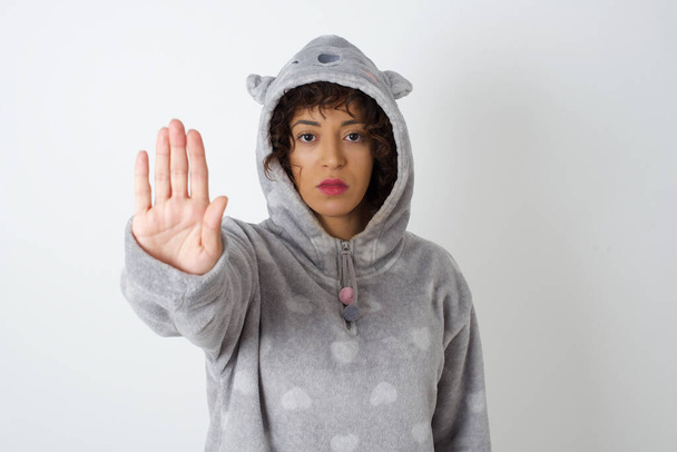 Mladá žena v pyžamu dělá zastavit gesto dlaní ruky. Výstražný výraz s negativním a vážným gestem na tváři izolované přes šedé pozadí. - Fotografie, Obrázek