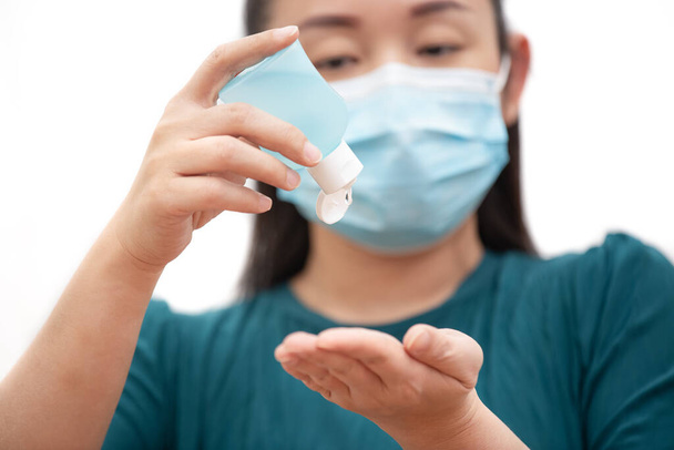 Nuoren aasialaisen naisen kuvapuoli pesee käsigeeliä ja käyttää naamiota bakteereiden, myrkyllisten höyryjen ja pölyn estämiseksi. Bakteeri-infektion ehkäisy ilmassa valkoisella taustalla - Valokuva, kuva