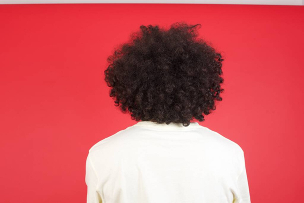 Młody mężczyzna z afro włosy na czerwonej ścianie, widok z tyłu  - Zdjęcie, obraz