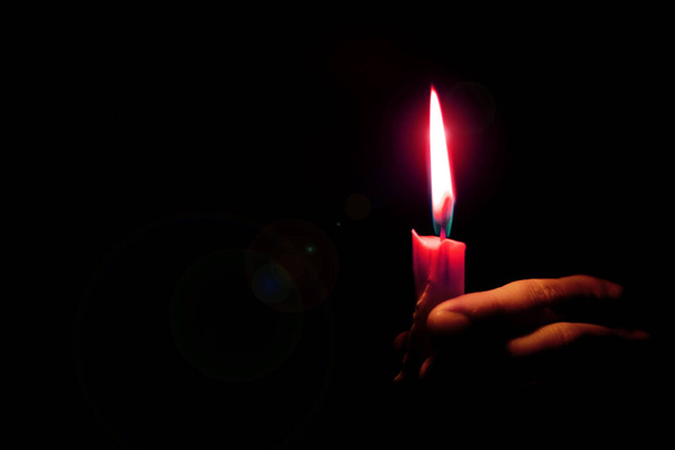 λάμψη από μια φλόγα κεριού φωτίζει το χέρι μιας γυναίκας σε ένα σκοτεινό δωμάτιο, θρησκεία - Φωτογραφία, εικόνα