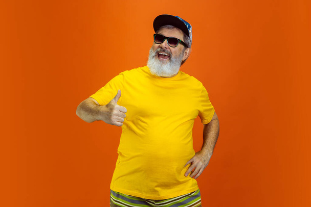Senior hipster man wearing eyeglasses posing on orange background. Tech and joyful elderly lifestyle concept - Фото, изображение