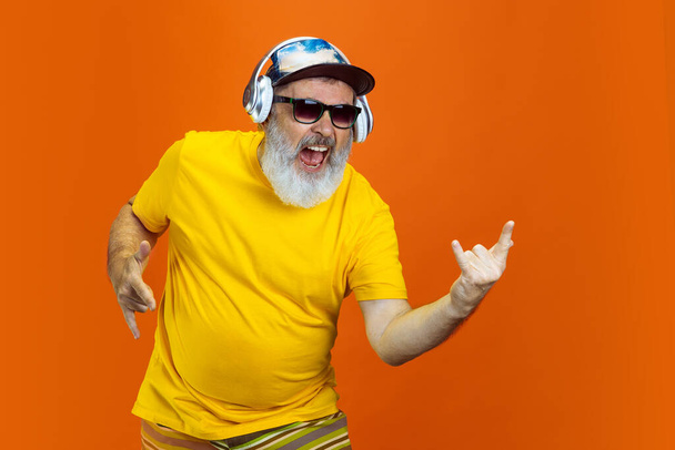Senior hipster man using devices, gadgets on orange background. Tech and joyful elderly lifestyle concept - Фото, изображение