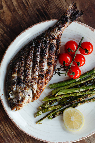 Grilled dorado fish with tomatoes, lemon and asparagus on a plate. Cooking recipe. - Photo, Image