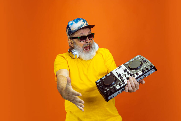 Senior hipster man using devices, gadgets on orange background. Tech and joyful elderly lifestyle concept - Zdjęcie, obraz