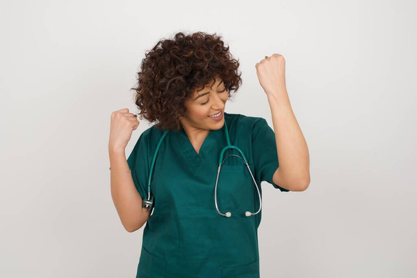  doctora vistiendo uniforme médico apretando sus puños con alegría feliz de lograr su objetivo y metas. Emociones positivas, sentimientos. - Foto, imagen