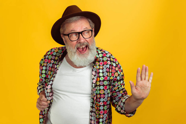 Senior hipster man wearing eyeglasses posing on yellow background. Tech and joyful elderly lifestyle concept - Fotografie, Obrázek