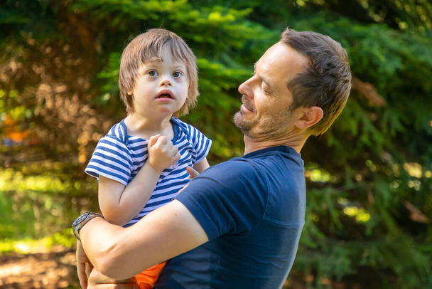Retrato de lindo bebé con síndrome de Down jugando con papá en el día de verano en la naturaleza - Foto, Imagen