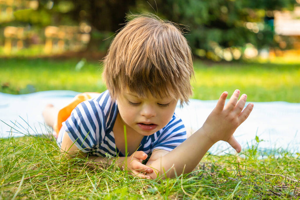 Portrait of Cute baby boy with Down syndrome playing in summer day on nature - Photo, Image