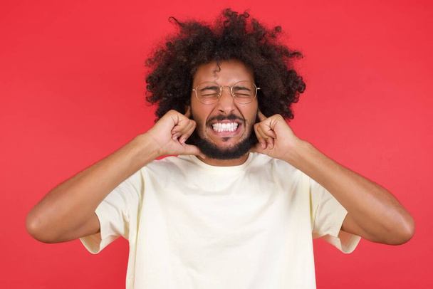 Young man with afro hair  closing ears     against red  wall  - Photo, Image