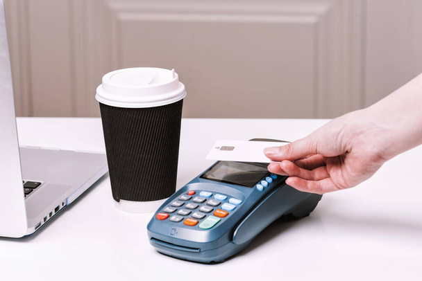 Woman pay by card. NFC payment terminal and take away cup of coffee with chocolate muffin on a white table. Credit card or phone pay pos banking device, card machine. - Photo, Image