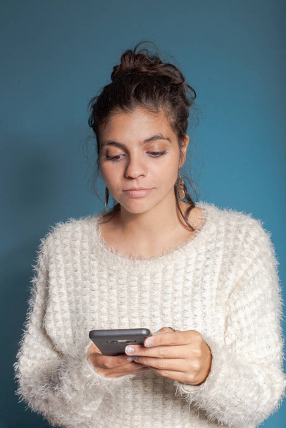 young woman in light clothes with light blue background with cell phone in hand - Foto, Imagem