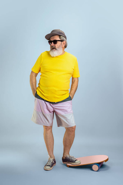 Senior hipster man wearing eyeglasses posing on light blue background. Tech and joyful elderly lifestyle concept - Foto, imagen