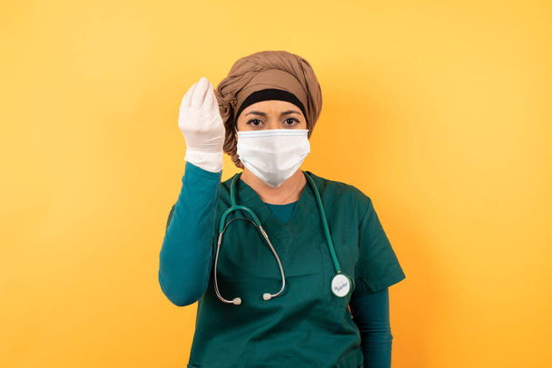 What the hell are you talking about. Shot of frustrated Young beautiful Muslim doctor woman in green medical uniform gesturing with raised hand doing Italian gesture, frowning, being displeased and confused with dumb question. - Zdjęcie, obraz