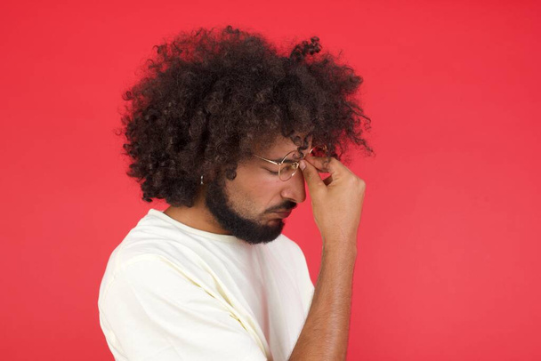 Νεαρός άνδρας με αφρο μαλλιά σκέφτεται ενάντια στον κόκκινο τοίχο  - Φωτογραφία, εικόνα
