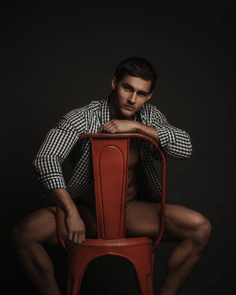 Handsome male model in only shirt sitting on red chair - Fotó, kép