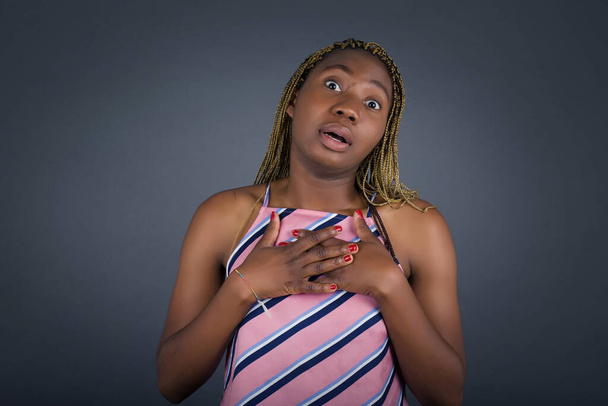 Junge emotionale afrikanisch-amerikanische Frau, die vor grauem Studiohintergrund steht, hat die Hände auf der Brust in Herznähe.  - Foto, Bild